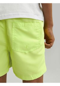 Pantalones cortos verde neón hechos de una tela ligera, con un bolsillo trasero con solapa rectangular y detalles de costura. Longitud a mitad del muslo.