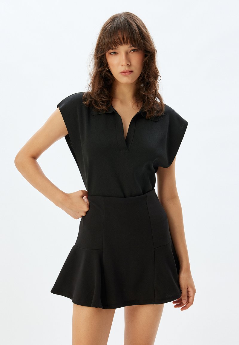 Blusa negra de manga corta con cuello, combinada con una falda negra de corte acampanado. Ambas prendas tienen una textura suave y un diseño minimalista.