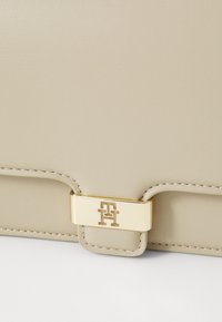 Beige bőr táska sima felülettel, arany színű csattal, amelybe vésett logó van, valamint kontrasztos varrási részletekkel.