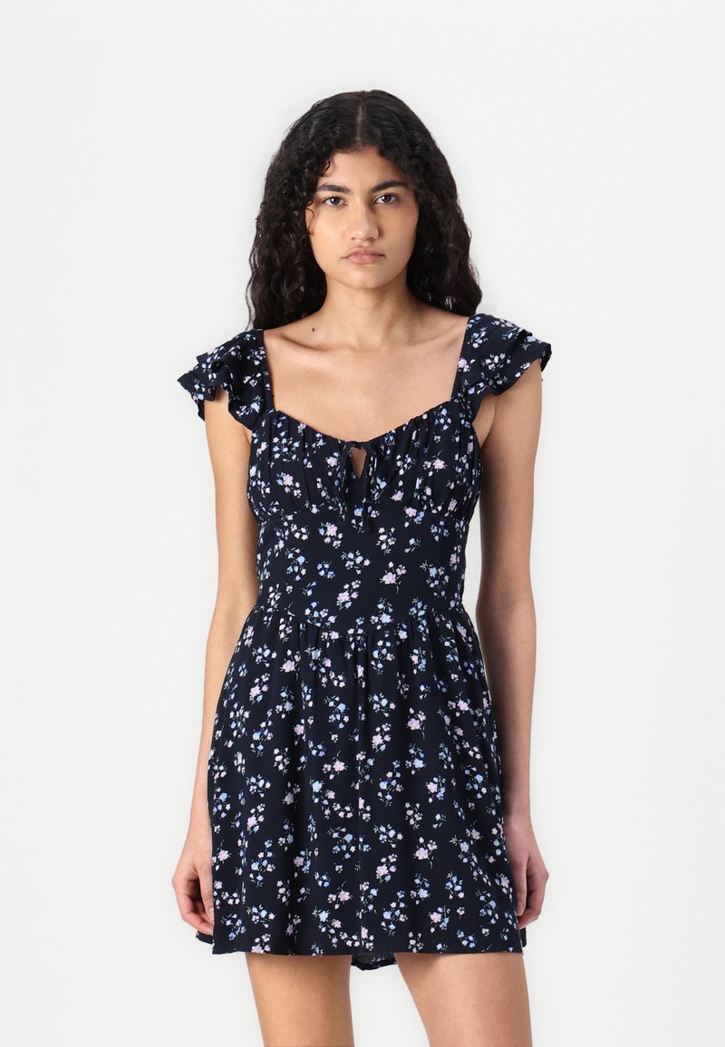 Vestido floral marino con un corpiño ajustado y mangas rizadas. Presenta un detalle de ojal y una falda acampanada con un delicado patrón floral.