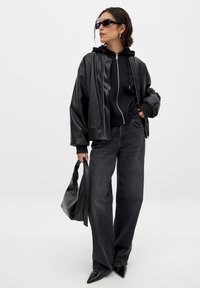 Black faux leather jacket over a black zip-up hoodie, paired with dark jeans and pointed black heels. Accessories include a black bag.