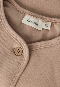 Ljusrosa bomullsskjorta med rund halsringning, knäppning med träknappar och sydda detaljer runt kragen och knappslån.