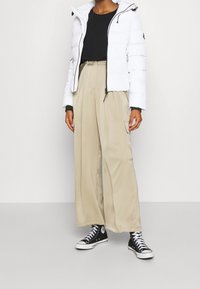 Hvid dunjakke med lynlås, sort langærmet top, beige bukser med vide ben og sorte høje sneakers.