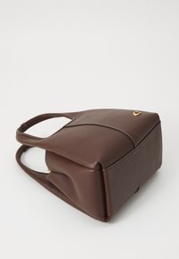 Bolso de mano de cuero marrón con dos asas, base estructurada y un pequeño detalle dorado en la esquina superior, colocado sobre una superficie blanca.