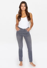 Grijze denim jeans met een slim fit, voorzien van een knoopsluiting, riemlussen en voorzakken. Model is gecombineerd met een witte tanktop.