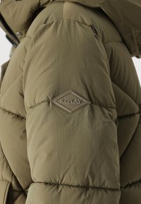 Grüne Puffjacke mit gestepptem Muster und glänzendem REPLAY-Logo auf der Schulter. Das Material wirkt glatt und langlebig.