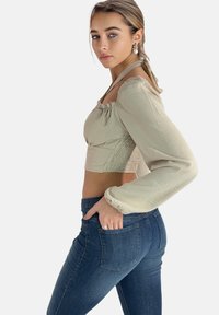 Hellgrünes, kurz geschnittenes Oberteil mit Puffärmeln, strukturiertem Stoff; kombiniert mit enganliegenden dunkelblauen Jeans mit Gesäßtaschen.