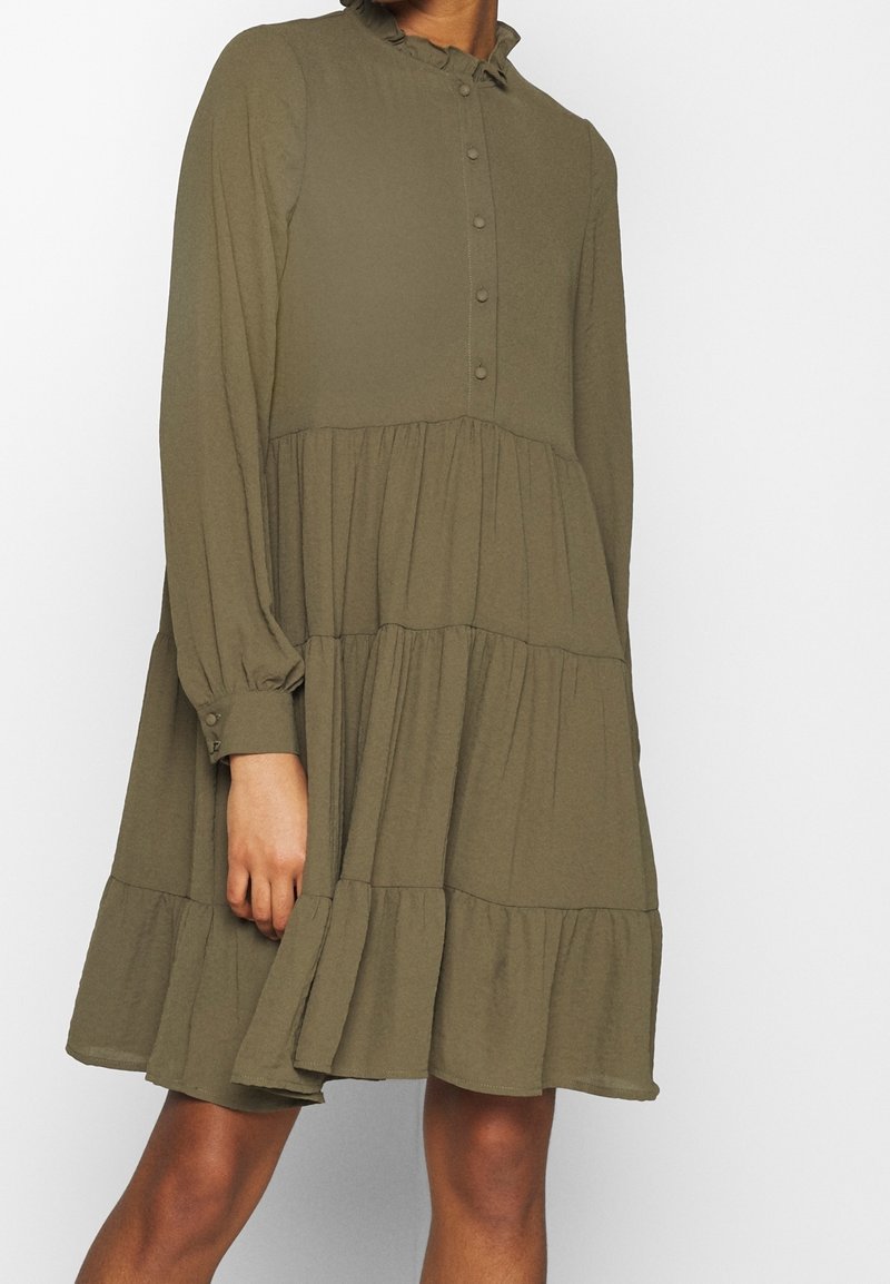 Robe verte olive, à plusieurs niveaux, avec des manches longues, un col froncé et un devant à boutons. Fabriquée en tissu doux avec une silhouette fluide et texturée.