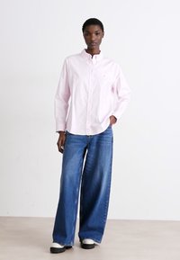 Camicia button-up a maniche lunghe di un rosa chiaro abbinata a jeans in denim blu a gamba larga. L'outfit presenta una vestibilità rilassata e un colletto.