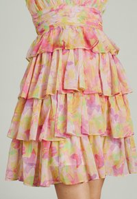 Gestuftes Kleid aus leichtem Stoff, mit Pastellfarben und floralen Mustern, Rüschensaum und taillierter Passform.