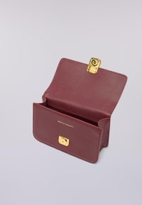 Burgundské kožené kabelky s hladkou texturou, zlatým kováním na závěsu a embosovaným logem "GENTLE SOCIETY" na přední straně. Otevřený design.