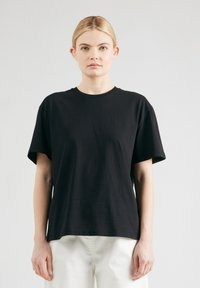 Zwarte katoenen T-shirt met een ronde hals, korte mouwen en een ontspannen pasvorm. Gladde textuur en eenvoudig ontwerp, weergegeven op een neutrale achtergrond.