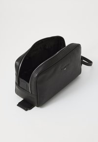 Beauty case in pelle nera con apertura a zip, superficie texture e una piccola maniglia laterale per un facile trasporto. Interno rivestito in tessuto nero.