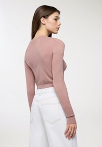 Różowy sweter z prążkowanego materiału, z długimi rękawami i dopasowaną talią. Połączony z białymi dżinsami z wysokim stanem, z minimalną ilością detali. 