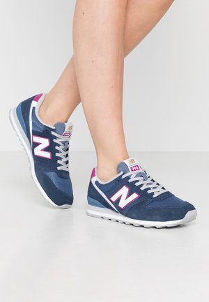 Baskets en daim bleu et en mesh avec une semelle blanche, arborant un grand logo "N" rose, des lacets gris et un accent rose sur le talon.