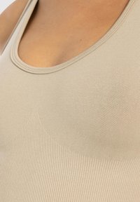 Primo piano di una persona che indossa una canottiera ribattuta beige con scollatura a barca.