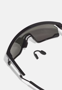 Ochelari de soare negri cu un design curbat, având lentile tintate și o finisare elegantă, netedă. Include o piesă de accent neagră, detașabilă.