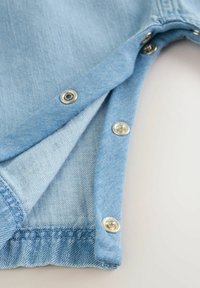 Ljusblå denimtyg med en tryckknapp vid öppningen, som visar en slät textur och prydliga sömmar längs kanterna.