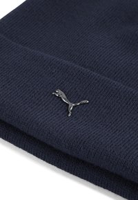 Mørkeblå strikket beanie med ribbet tekstur og en foldet kant, der har et metallisk sølvfarvet Puma-logo på forsiden til branding.