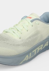 Chaussure de course jaune clair avec empeigne en mesh, lacets jaunes, semelle grise et marquage "ALTRA" sur le côté.