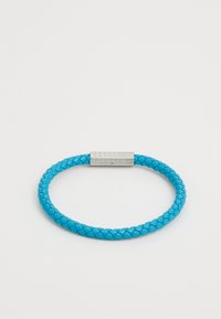 Pulsera de cuero trenzado en color turquesa con un cierre magnético plateado texturizado. Diseño circular, textura suave y color vibrante.