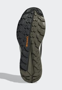 Rubber shoe sole featuring a tread pattern with varying depths in black and olive green, with an orange Continental logo on the side.