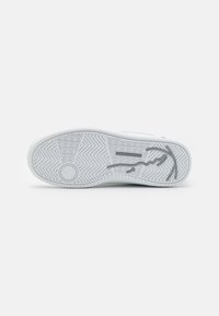 Hvit såle på sneakers med zigzag-mønster. Merkbar grå logo-trykk og sirkulært designelement nær hælen. Teksturert detaljering.