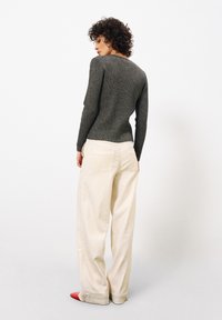 Grauer, taillierter Pullover mit strukturierter Oberfläche, kombiniert mit locker sitzenden, cremefarbenen Hosen und roten spitzen Ballerinas, von hinten betrachtet.