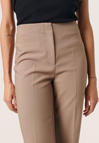Beige kankaat, joissa on sileä pinta, korkea vyötärö ja etusaumayksityiskohdat. Yhdistetty mustaan ribbipaitaankaan.