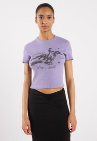 Purple ribbed cropped t-shirt with short sleeves, featuring a black graphic design of a horse and text "Stay Wild," paired with a black fitted skirt.