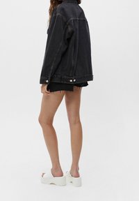 Giacca di jeans nera, vestibilità morbida, con colletto e chiusure a bottone. Abbinata a pantaloni corti neri strappati e sandali bianchi con tacco alto.