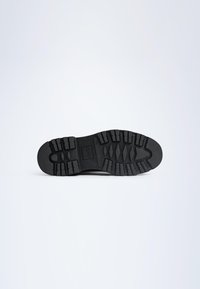 Black rubber shoe sole featuring deep treads for traction, textured surface, and a rounded toe. No visible branding or patterns.