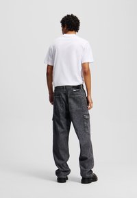 Cargo bukser i mørk denim med en løstsiddende pasform, flere baglommer og kontrastsyninger, parret med en ensfarvet hvid T-shirt med korte ærmer.