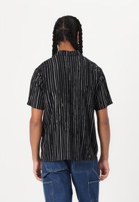 Short-sleeve black shirt with vertical white stripes, a relaxed fit, a back yoke detail, and a subtle collar for casual wear.