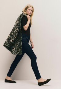 Leoparda raksta mētelis, tumši pieguļošas džinses un melnas plakanās kurpes. Mētelim ir teksturēta auduma virsma un tas ir pārmetīts pāri plecam.