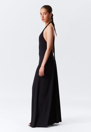 Black halter-neck maxi dress with a fitted bodice, open back, and flowing skirt. Smooth, lightweight fabric showcases a sleek silhouette.