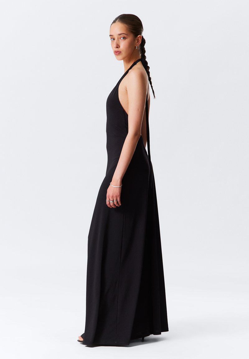 Crna halter-kragna maxi haljina s uskim korzetom, otvorenim leđima i lepršavom suknjom. Glatka, lagana tkanina prikazuje elegantnu siluetu.