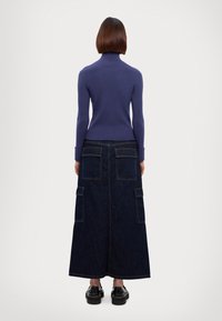 Paarse geribde coltrui gecombineerd met een lange donkerdenim rok met twee grote achterzakken en contrasterende stiksels.