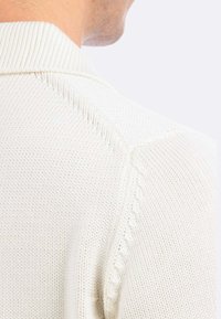 Maglione di lana di colore crema chiaro con tessuto testurizzato, colletto a costine e un motivo decorativo lungo la cucitura della spalla.