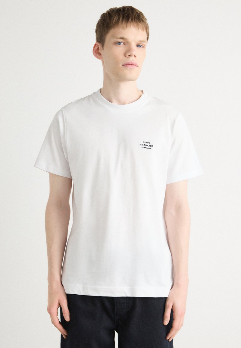 Hvid bomuld t-shirt med rund hals, korte ærmer, og et lille sort logo trykt på venstre bryst. Simpelt design, standard pasform.