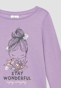 Lavender langemouwen T-shirt met ronde hals. Aan de voorkant staat een afdruk van een meisje omringd door bloemen en de tekst: "BLIJF WONDERLIJK, geniet elke dag."