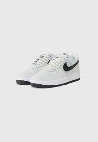 White leather sneakers with black swoosh, round toe, perforated design, white sole, and blue accents on the tongue.