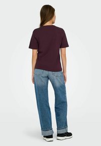 T-shirt bordeaux con maniche corte, abbinato a jeans larghi di colore blu chiaro. Sneakers nere con suola bianca completano l'outfit.
