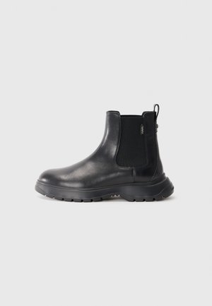 Bottines Chelsea en cuir noir avec panneaux latéraux élastiques, bout rond, semelle en caoutchouc texturé et une languette à l'arrière pour un enfilage facile.