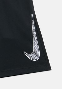 Fekete atlétikai rövidnadrág texturált felülettel, nagy fehér Nike logóval, amely csíkos mintázattal díszített az alsó bal oldalon.