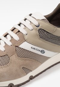 Brązowy i beżowy sneaker z siateczkowych i zamszowych materiałów. Posiada białe akcenty i sznurowadła, zaokrąglony nosek oraz logo po boku.