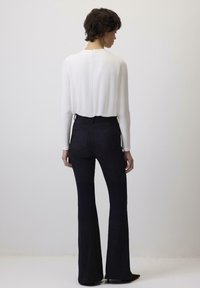 Witte lange mouwen top met een ronde halslijn en sluiting aan de achterkant, gecombineerd met hoge zwarte flared jeans. Glad aanvoelende textuur en aangesloten ontwerp.