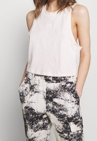 Ljusrosa ärmlös crop top i mjukt tyg med rund halsringning och liten vit logotyp. Matchad med mönstrade svarta och krämfärgade byxor med fickor.