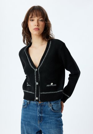 Gilet en maille noire avec un profond décolleté en V, des boutons à fermeture argentée, des détails de couture contrastants et deux poches avant.