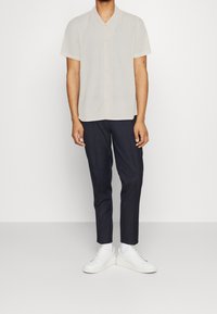 Korteblauwe, lichtbeige shirt met een knoopsluiting, gecombineerd met donkere, op maat gemaakte broeken en witte sneakers. Eenvoudige en moderne esthetiek.